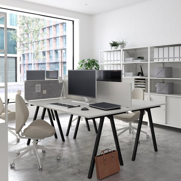 Modern kantoor met twee TROTTEN-bureaus, computers en een raam met uitzicht op de stad.