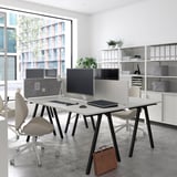 Modern kantoor met twee TROTTEN-bureaus, computers en een raam met uitzicht op de stad.