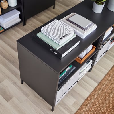 Zwarte troffenkast met schuifdeuren die de ruimte verdelen, op houten vloer, met boeken, dienblad.