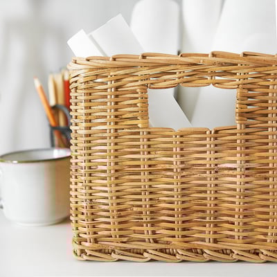 Rieten mand met houten handvatten, met daarin wit papier, op wit oppervlak.