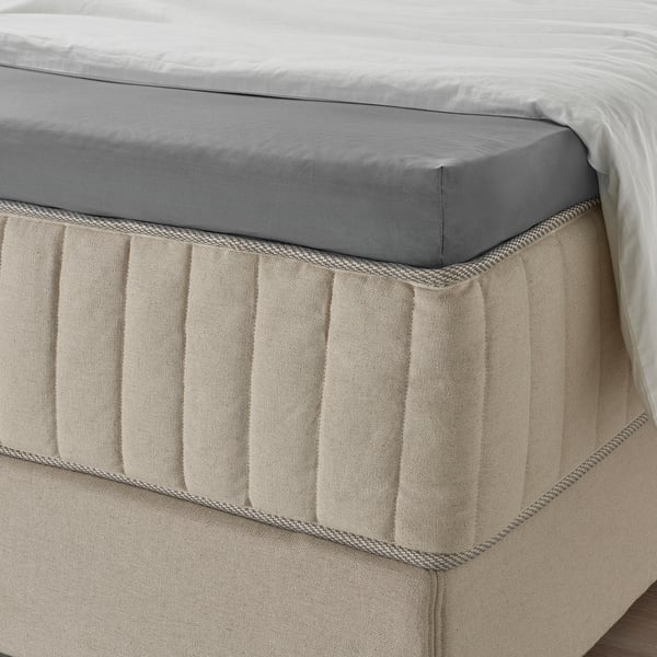 Bed met grijs hoeslaken, beige linnen rok met textuur, elastische rand, ziet er zacht en ademend uit.