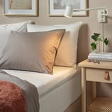 Grijze beddengoed set met klein nachtkastje en decor.