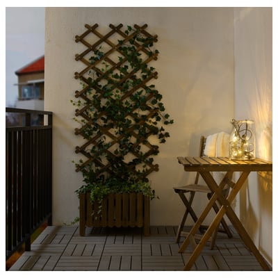 Gezellig balkon met houten tafel, stoel, UTSUND-verlichting en plantenlatwerk.