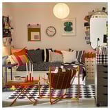 Lichte slaapkamer met zwart gestippeld vloerkleed, kleurrijke kussens, wandklok, hanglamp, kunst aan de muur en oranje meubels.