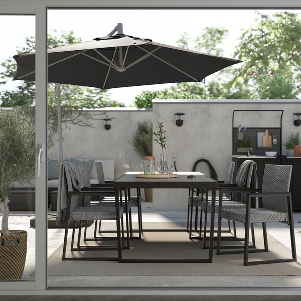 Buiten eethoek met zwarte metalen tafel en stoelen, grote parasol voor schaduw, omgeven door betonnen muren en groen.