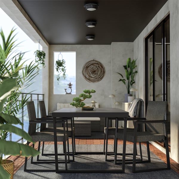 Moderne patio zwart metalen eethoek met rieten stoelen, omgeven door weelderig groen, onder een overdekte ruimte met inbouwverlichting.