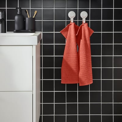 Rode VÅGSJÖN handdoeken hangen aan zwart betegelde muur, witte gootsteen links.