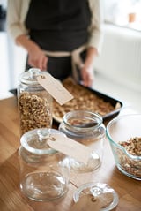Een persoon kookt granola in een pan op een houten aanrecht met gelabelde potten zelfgemaakte granola.