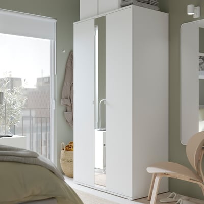 Moderne slaapkamer met witte VIHALS kledingkast met passpiegel, houten stoel en groene wanden.