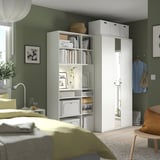 Slaapkamer met groene muren, witte meubels: bed met groene deken, rekken en kledingkast met spiegel.