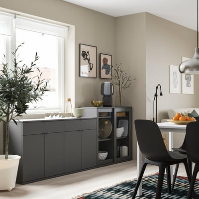 Moderne eetkamer met grijze kast en zwarte stoelen, kleurrijk tapijt en kunst aan de muur.