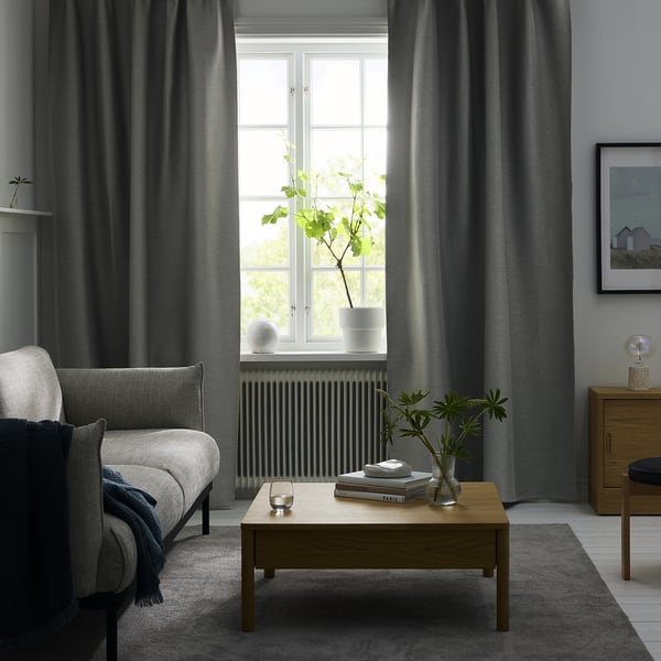Moderne woonkamer: grijze gordijnen, houten salontafel met boeken, witte fauteuil, grijs vloerkleed, groot raam.