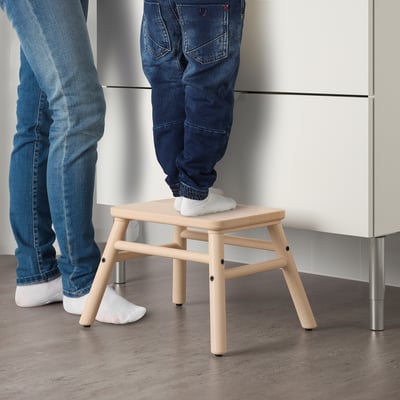 Twee mensen gebruiken een houten kruk, waarvan er één erop staat, waarschijnlijk om hogere delen te bereiken, om zijn functie als opstapje te demonstreren.