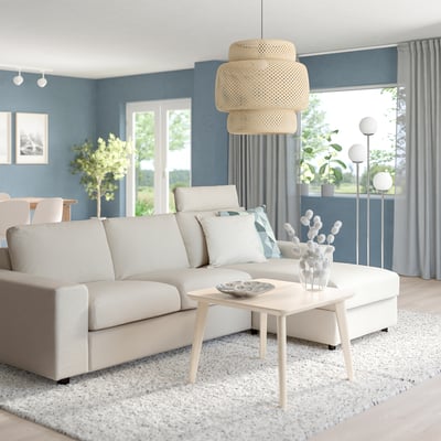 Beige l-vormige VIMLE sectionele bank met bijpassende salontafel, vaas en hanglamp tegen blauwe muur.
