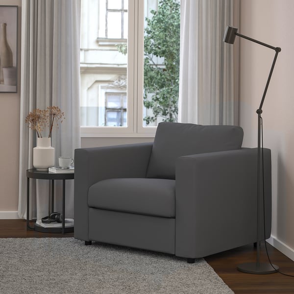 Gezellige grijze VIMLE fauteuil in moderne woonkamer met vloerkleed, vloerlamp en bijzettafel, bij groot raam.