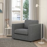 Moderne grijze VIMLE stoel, vierkante vorm. Geplaatst tussen groot raam en witte lamp, kleiner dan bijzettafel.
