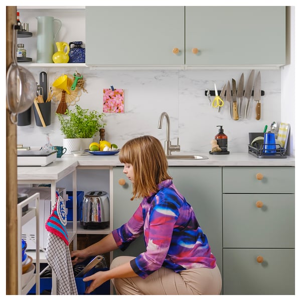 Moderne keuken met beige kasten, marmeren werkbladen. Vrouw die afwas, kruiden en gereedschap wast.