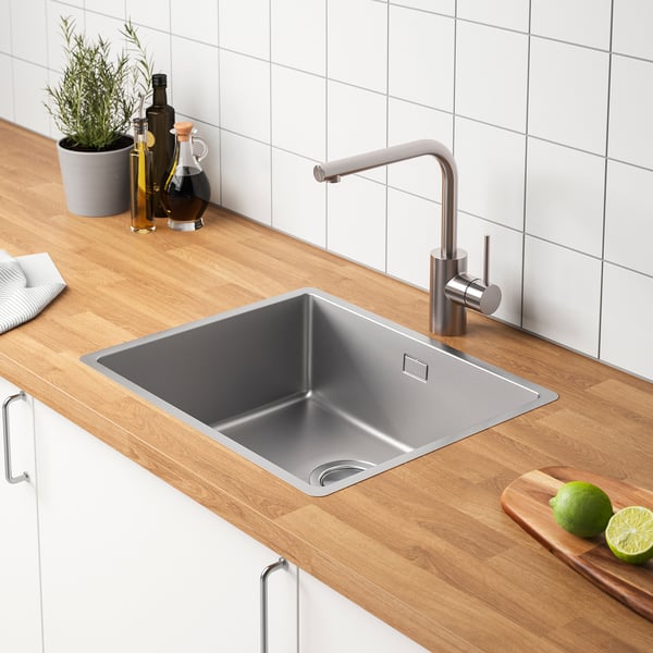 Moderne gootsteen met roestvrijstalen kraan, houten aanrechtblad en flessen, limoenen en plantendecor.