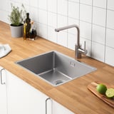 Moderne gootsteen met roestvrijstalen kraan, houten aanrechtblad en flessen, limoenen en plantendecor.