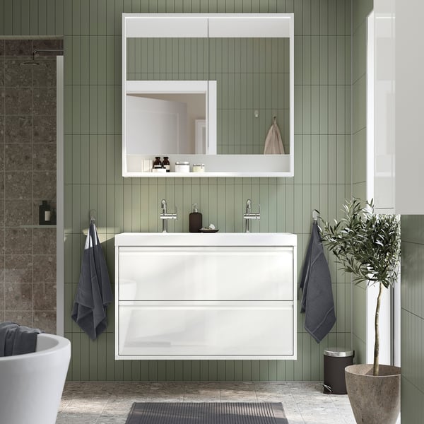 Modern white ÄNGSJÖN bathroom vanity with drawers, wall-mounted, green tiles, mirror, blue towels, plant.