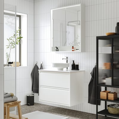 A modern white bathroom with a floating ÄNGSJÖN cabinet, a rectangular sink, and a big mirror. The cabinet is mid-sized compared to other items.