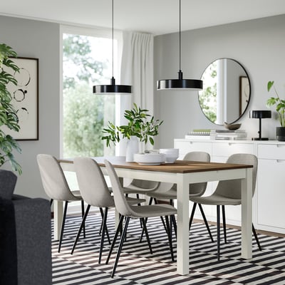 ÅLHULT dining set: extendable table, 6 grey chairs, plates, plant, 2 black pendants, round mirror, white sideboard, large window, colourful rug.