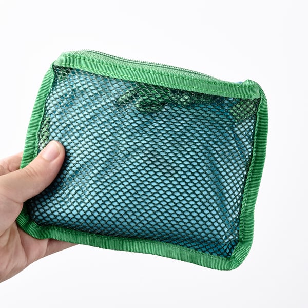 Hand holding green backpack with mesh pocket, ideal for beach or forest trips, with adjustable straps.