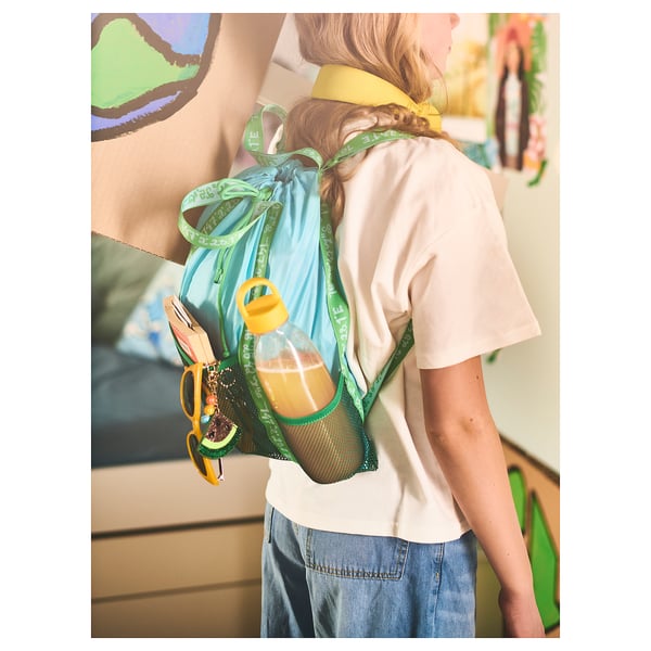 Person wears BLÅVINGAD backpack in blue and green. Its made of recycled polyester, has multiple pockets, and is suitable for outdoor activities.