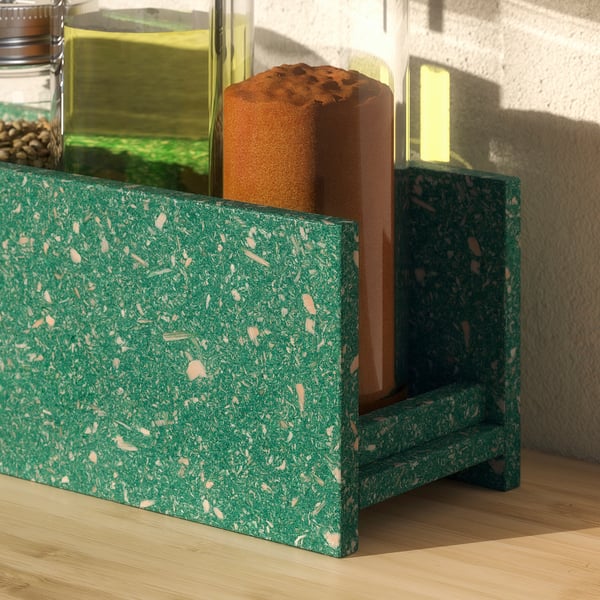 Green HUNDHAJ spice rack with speckled design, standing on a wooden floor, holding glass jars with food.