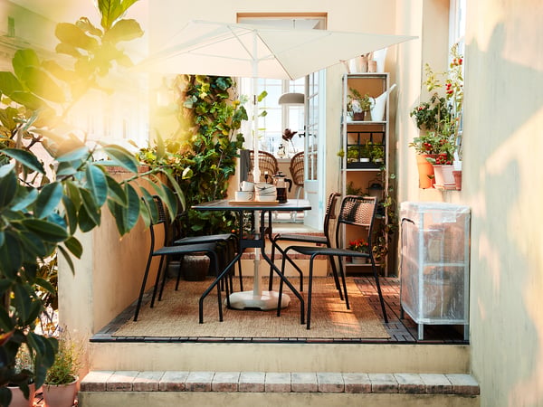 Small balcony with black metal table and chairs, white umbrella, and potted plants.