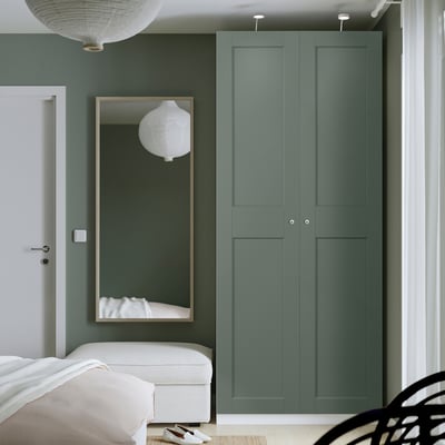 Modern bedroom with tall teal green PAX wardrobe. White bed & mirror beside it.