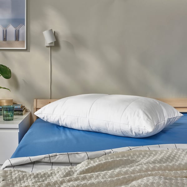 SENAPSMOTT pillow on bed, white, square, soft, with blue sheets, plant, lamp, books.