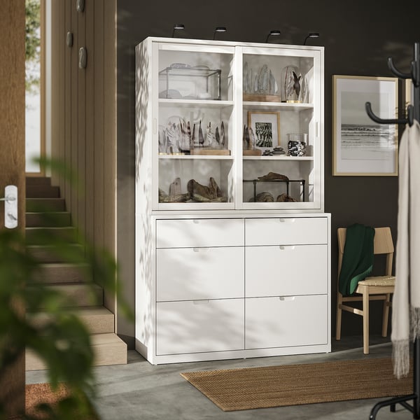Modern off-white cabinet with glass doors and drawers displays collectibles, featuring clean lines and soft-close drawers.