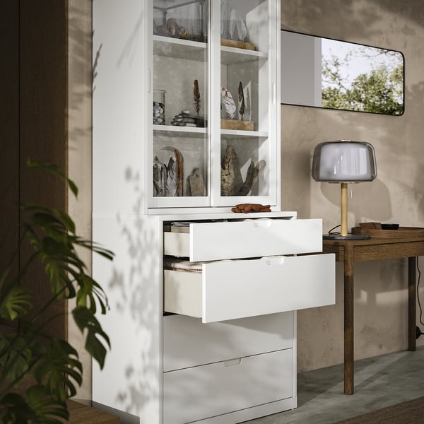 Modern room with white TONSTAD cabinet & chest, glass doors, wooden desk, lamp & plant.