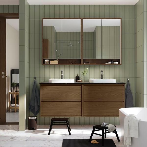 Modern bathroom with ÄNGSJÖN double vanity in brown oak. Mirrors, marble sinks, green tile walls. Spacious, coordinated design.