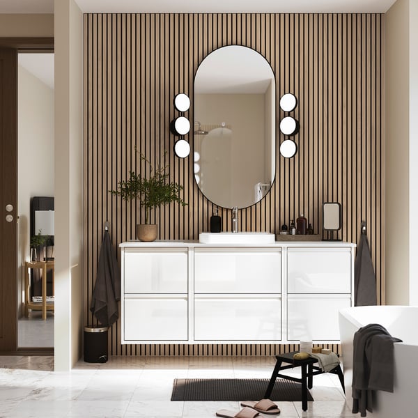 Modern bathroom with ÄNGSJÖN vanity, mirror, black accents. Marble sink, striped wall, stool, plant.