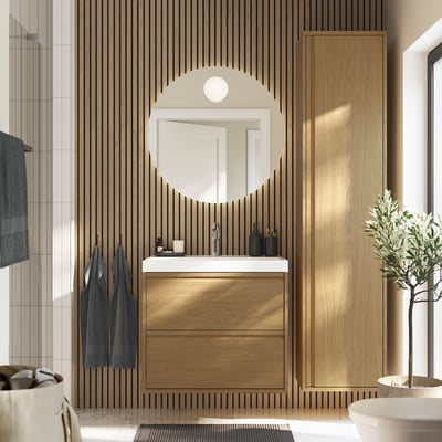 Modern bathroom with oak-brown vanity, sink, mirror, and wooden slats. Plant adds greenery.