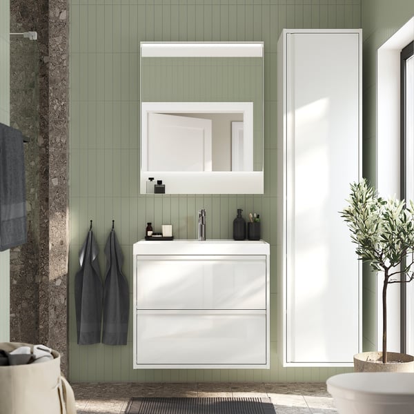 A modern bathroom with ÄNGSJÖN cabinet & sink. Green tiles, dark towels, olive tree.