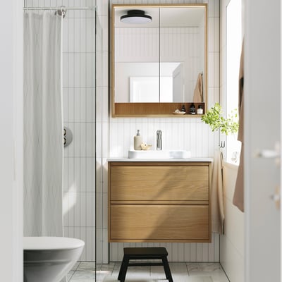 Modern bathroom with wooden vanity, white basin, mirror, glass shower. Light wood, minimal design, sleek handles.