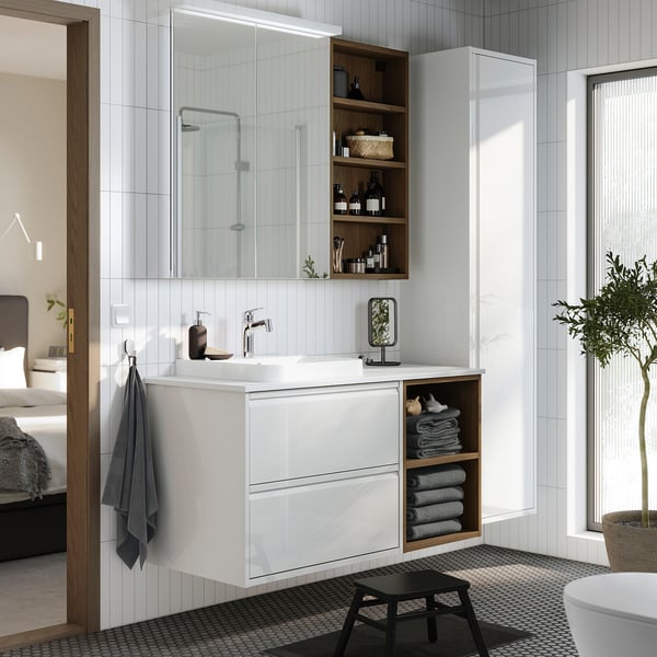 Modern white bathroom vanity with marble top, mirror, and black stool.