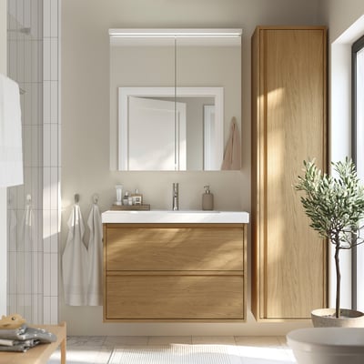 Modern bathroom with oak-brown vanity, mirror cabinet, white sink, plant.