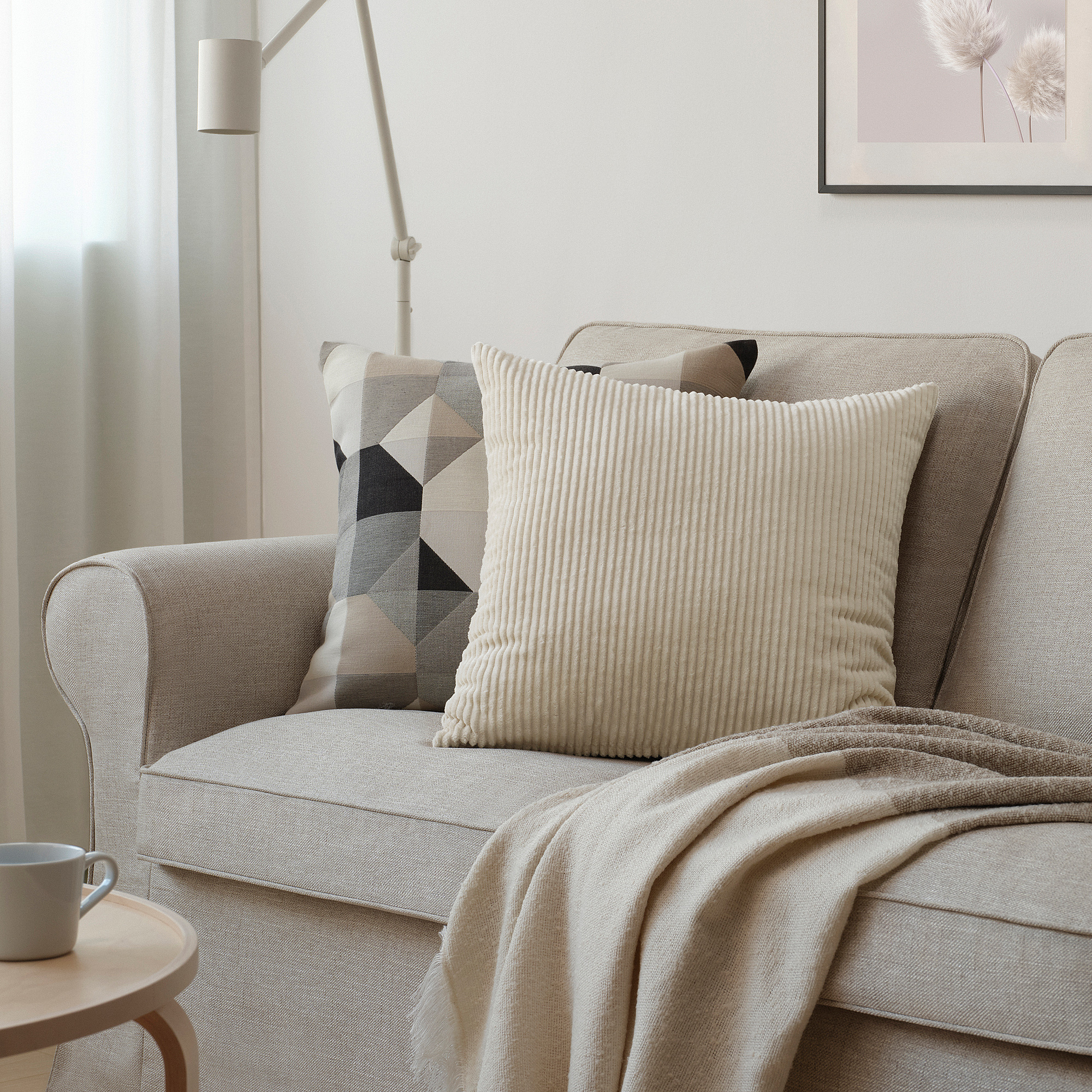 The ÅSVEIG beige corduroy cushion on a beige sofa. Its square-shaped with vertical lines, medium-sized among other items.
