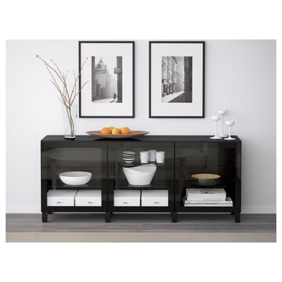 Black glass storage cabinet with tempered glass doors. Top has fruit dish, cups, and vase with branches. Wall-mounted, protects belongings from dust.