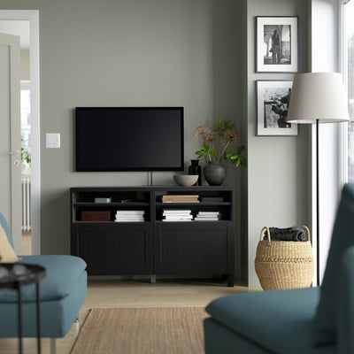 Modern living room: BESTÅ black tv bench with a large flat screen tv, framed pictures, blue couch, and wicker basket on a grey wall.