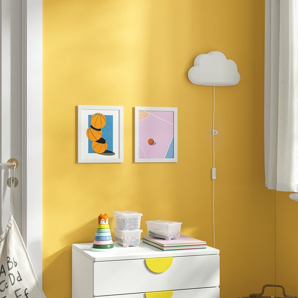 Two small pictures on yellow wall: left/basketballs, right/pink & orange. Nearby lamp, toys, yellow curtain.