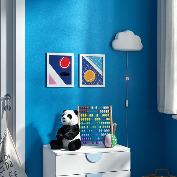Colourful geometric prints with sports balls hang above a white drawer in a blue room, featuring a panda, abacus, and cloud lamp.