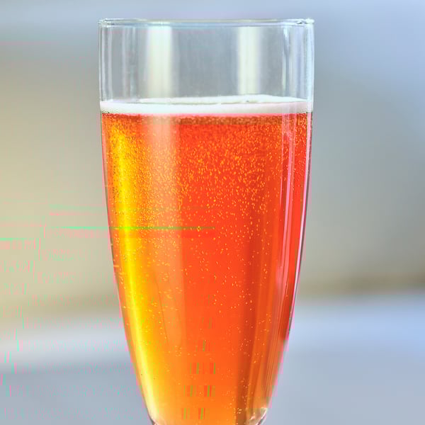 Tall, clear glass of orange-red bubbly drink, likely dryck bubble äppl & lingon, with a glowing gold hue.