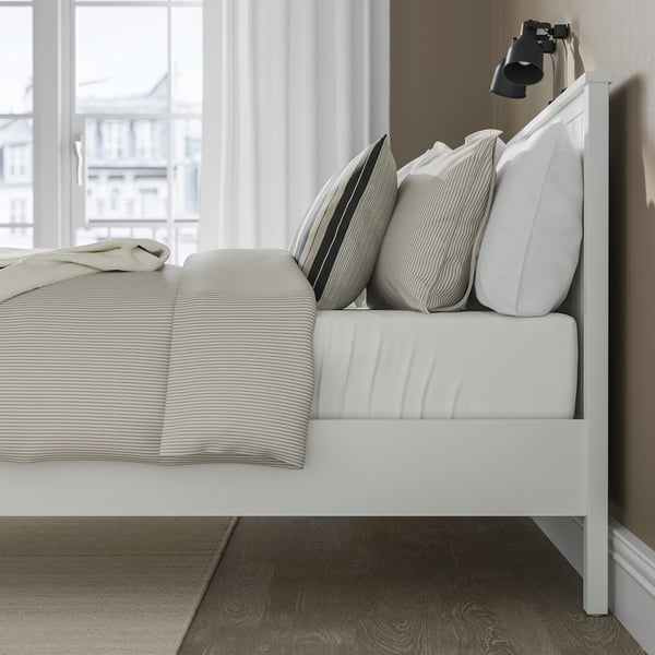 Bedroom scene with white GULLABERG bed, striped pillows, open window, curtains, rug, underbed storage space.