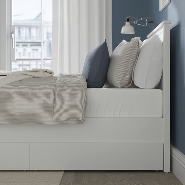 Tidy bed with striped linens and pillows. Under-bed storage drawers, blue wall, and wall lamp.
