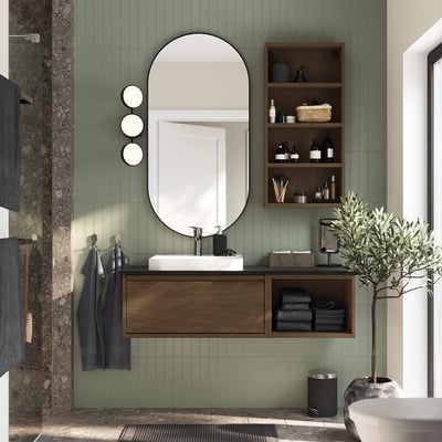Modern bathroom with brown wooden cabinet, towels, mirror, green tiles.